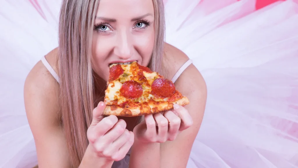 Giovane donna in tulle rosa morde una fetta di pizza al salame piccante
