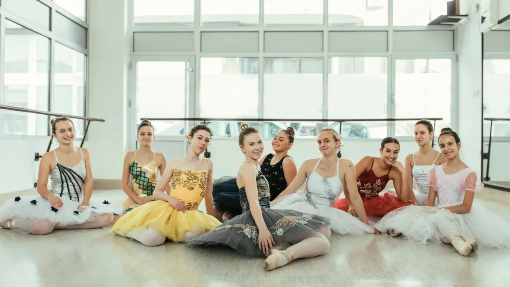 Gruppo di giovani ballerine in tutù sorridenti sedute insieme in una sala luminosa