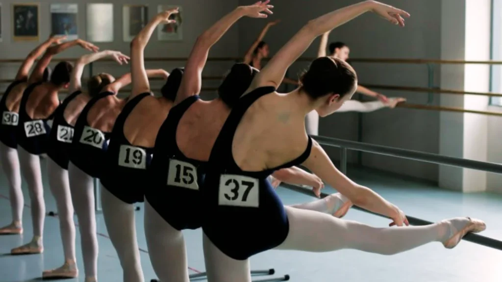 Ballerine con numero di gara eseguono esercizi alla sbarra durante un concorso di danza