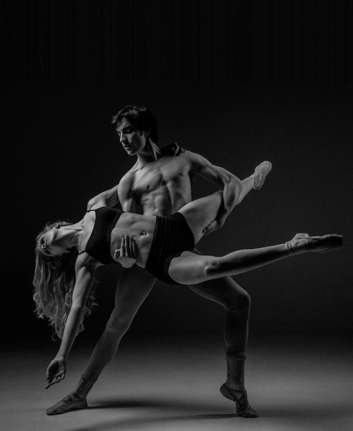 Coppia di ballerini di danza classica in un passo a due in bianco e nero su sfondo scuro da palcoscenico