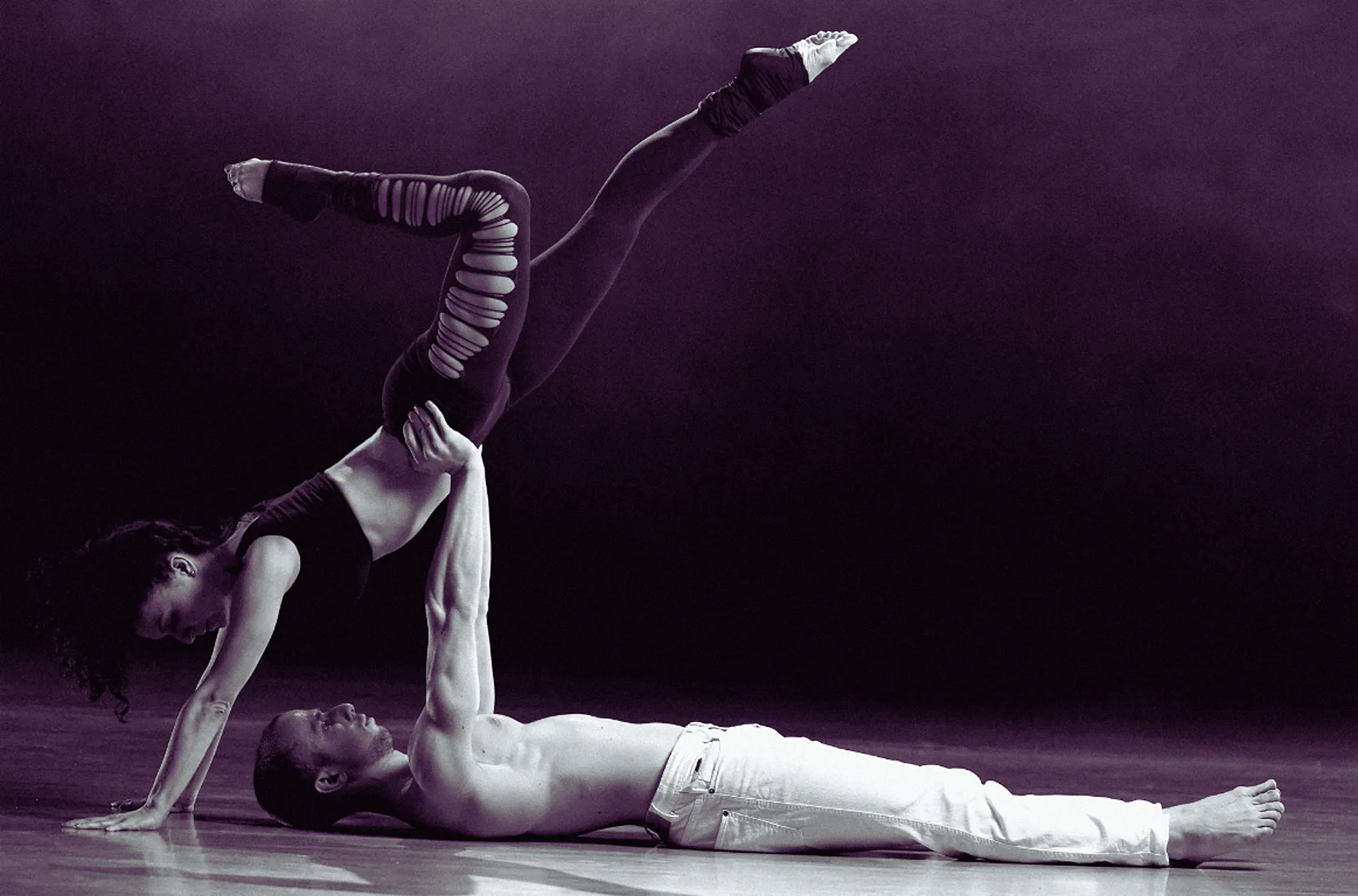 Coppia di danzatori contemporanei in una figura acrobatica a terra su palcoscenico scuro viola