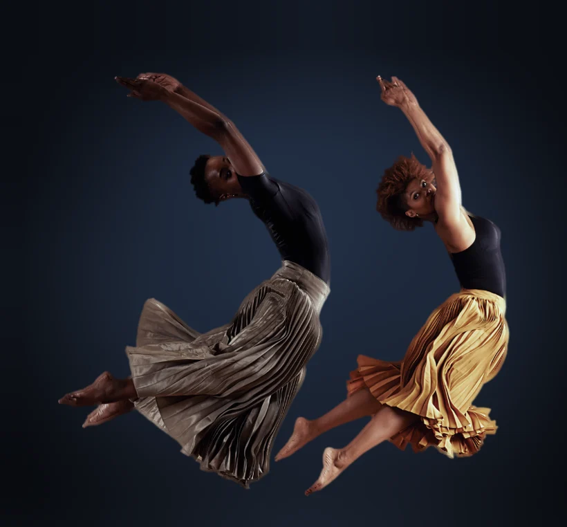 Due danzatrici in salto con gonne plissettate su sfondo scuro blu con luce soffusa
