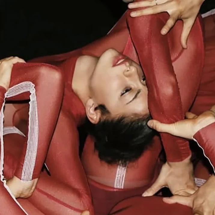 Danzatrice con costume rosso tra altri danzatori in una composizione di danza contemporanea
