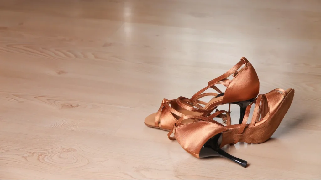 Scarpe da ballo in raso color bronzo con tacco appoggiate su parquet chiaro