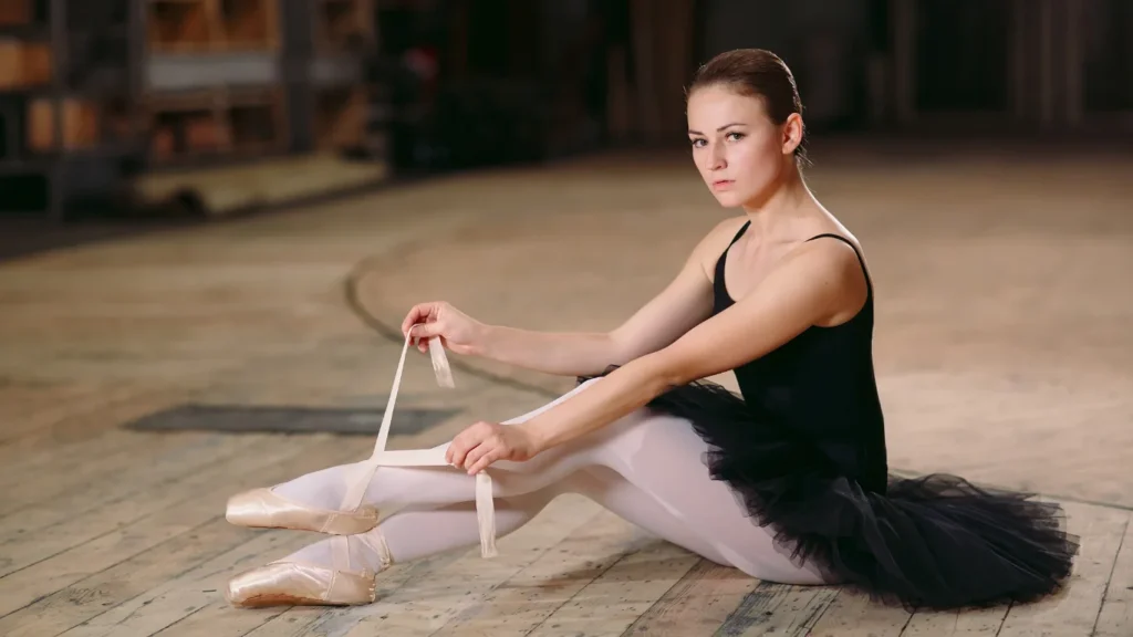 Ballerina in tutù nero seduta sul palco allaccia i nastri delle scarpette da punta